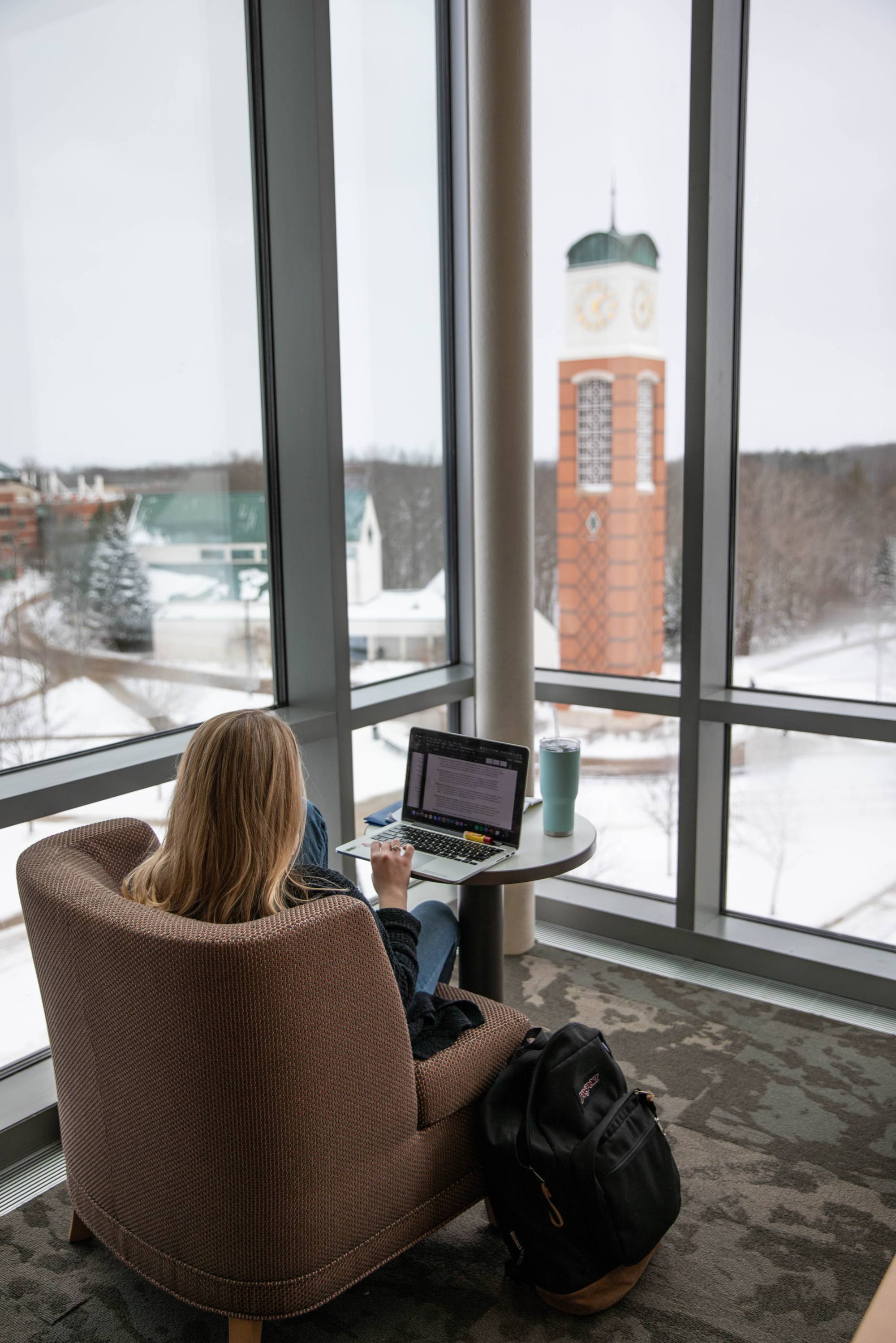 Student in Allendale library with computer and clock tower in background